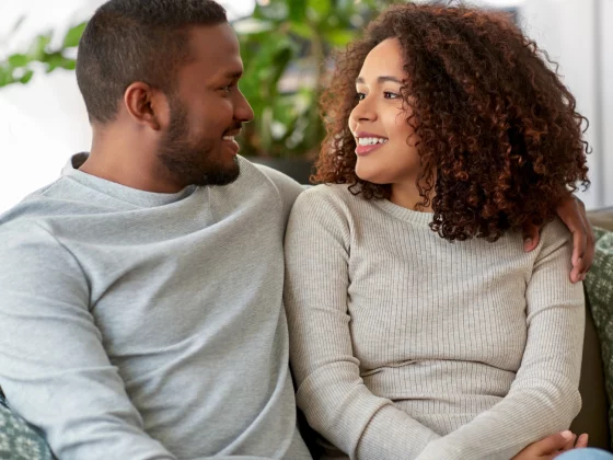 Man and woman sit next to each other on the sofa. The man has his arm around the woman.